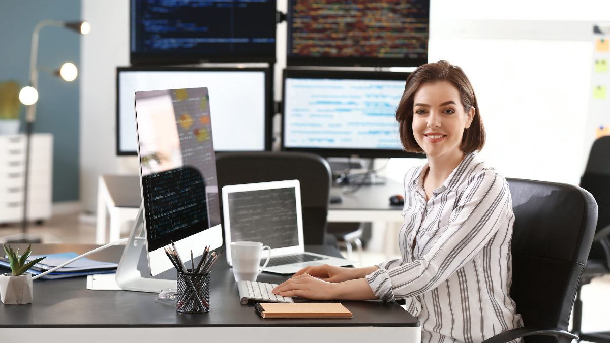 Programistka siedząca przy biurku w biurze z monitorami z kodem